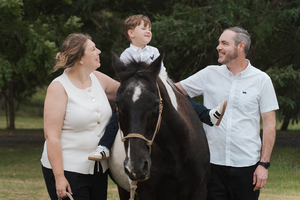 A family poses with their black horse in a grassy field during a family outdoor photo session in the gables