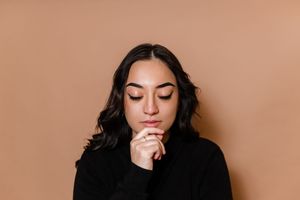 A person wearing black sits against a peach-colored wall in a series of moody portrait poses.