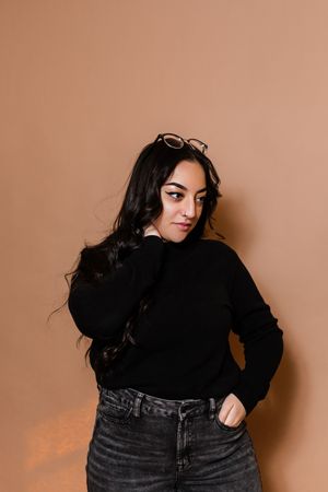 Fashion portrait series showing woman in black sweater and jeans posing against beige background.