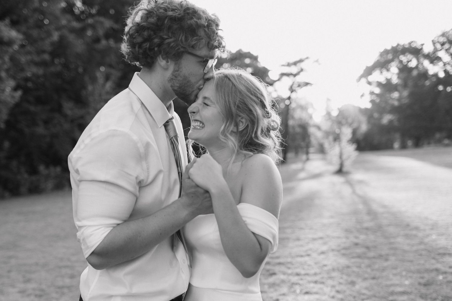 Young newly wed couple embracing with hands intertwined. The sunset is shining through the trees and the bride is smiling from ear to ear.