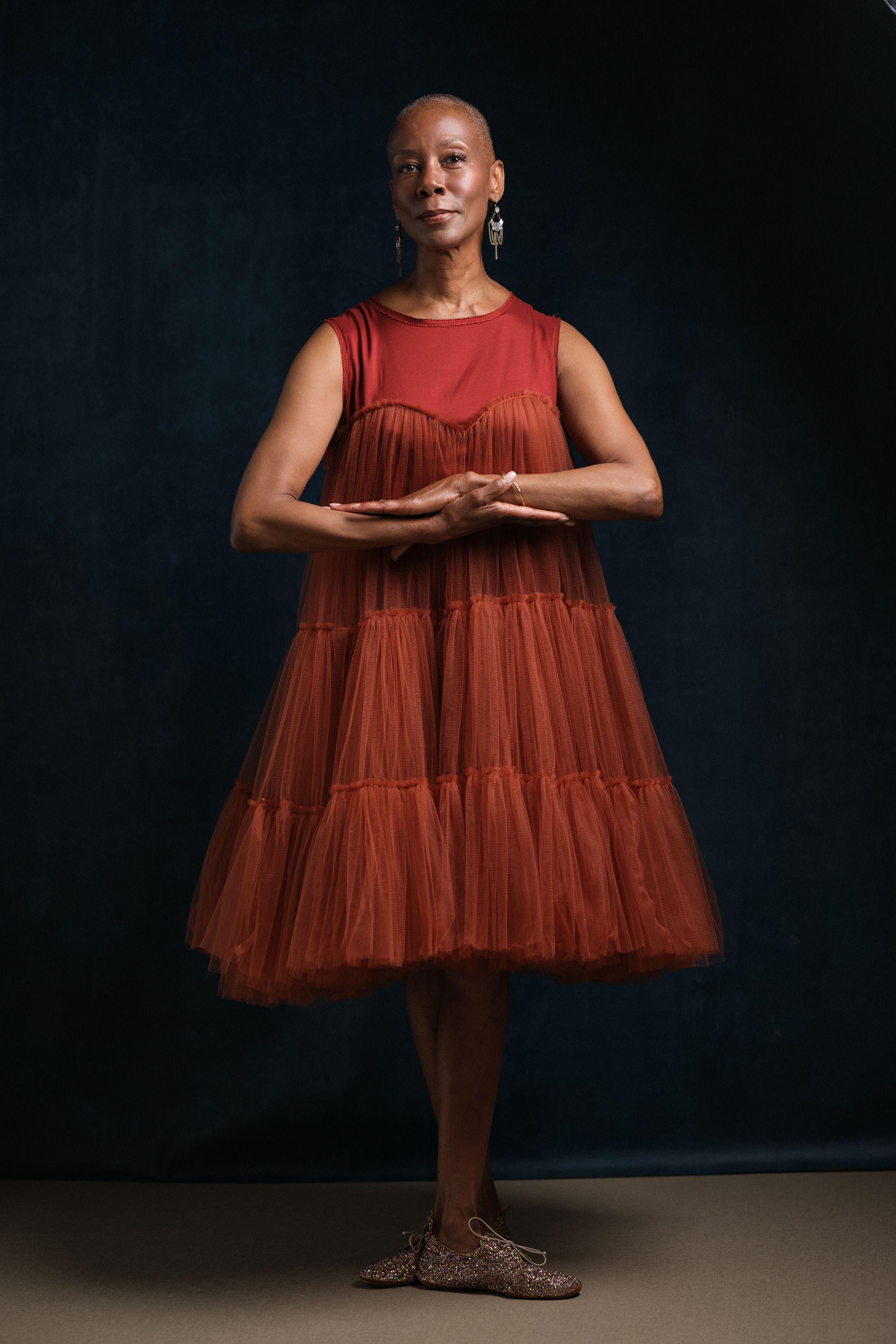 Full-length portrait in flowing red tiered dress against dark backdrop.