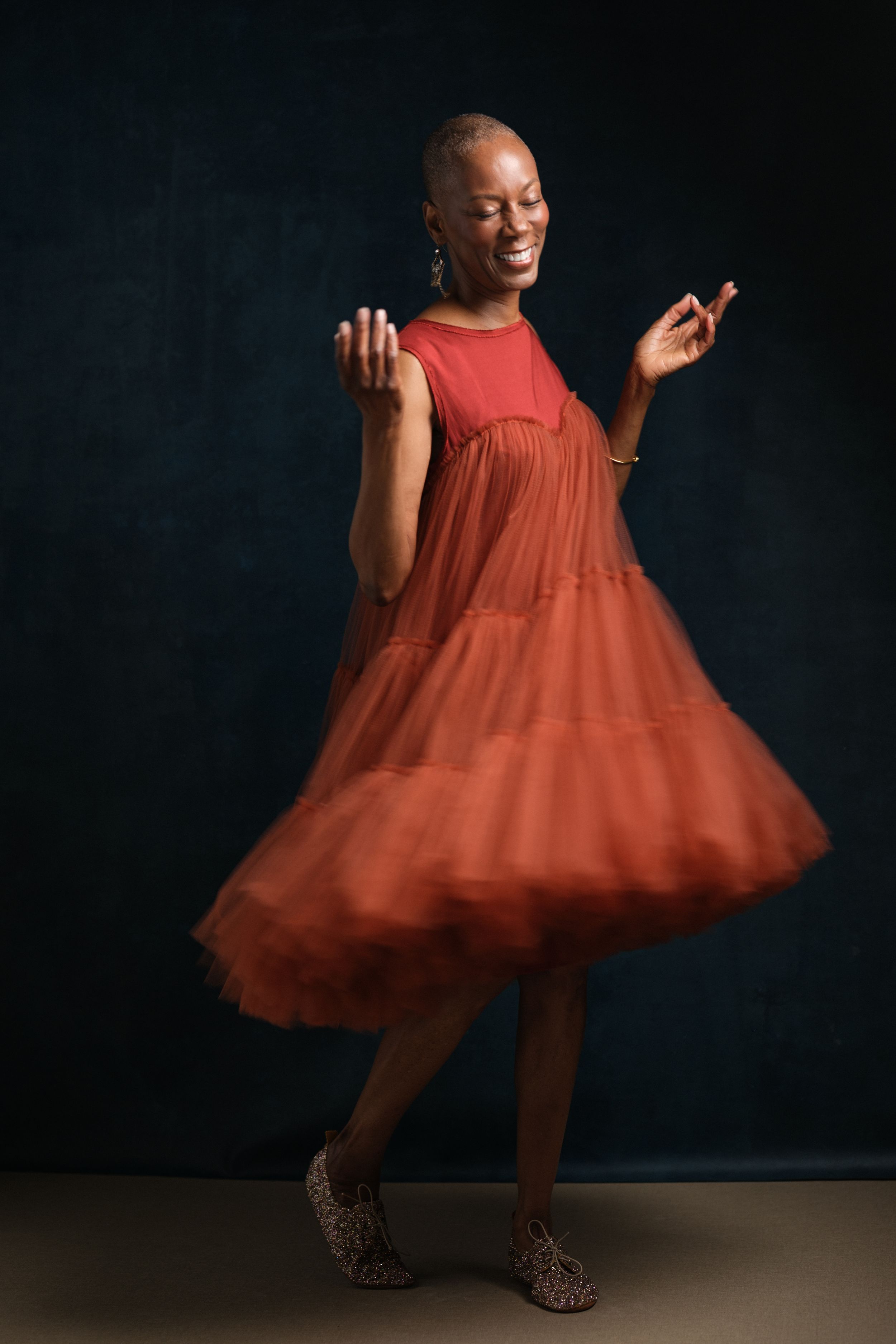 Joyful movement captured in twirling red tulle dress against dark background.