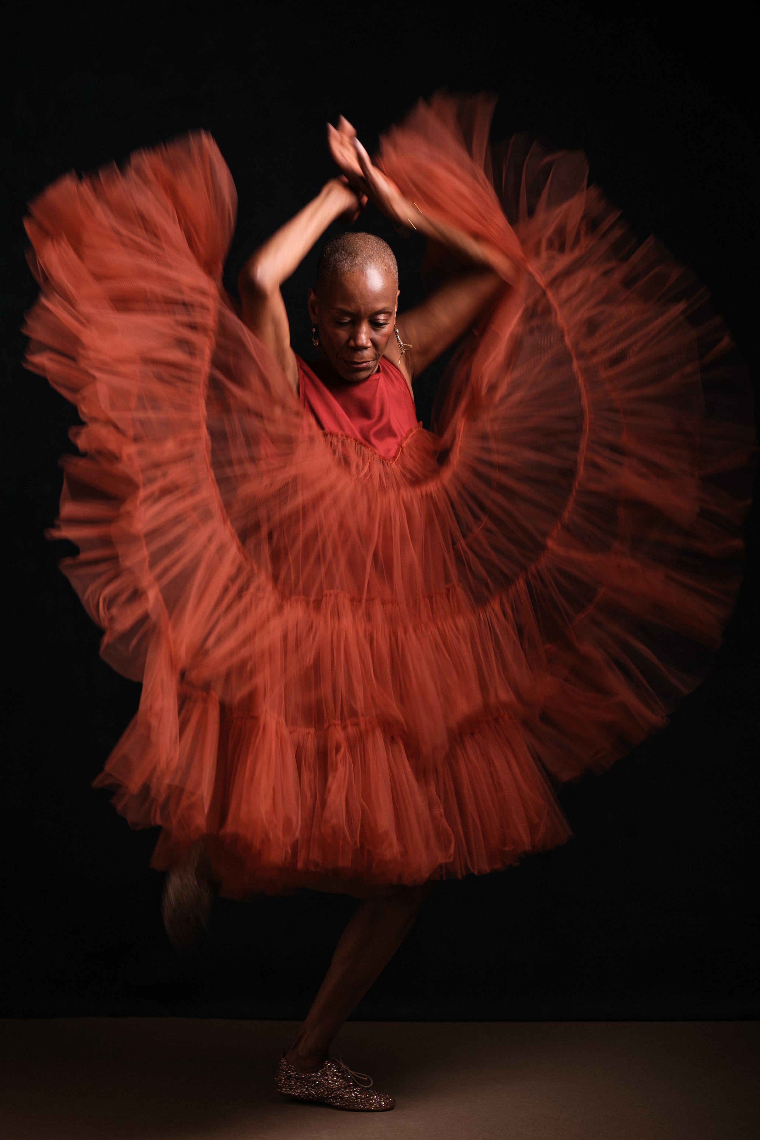 Dancer twirling in a voluminous red dress creates circular patterns against dark backdrop.