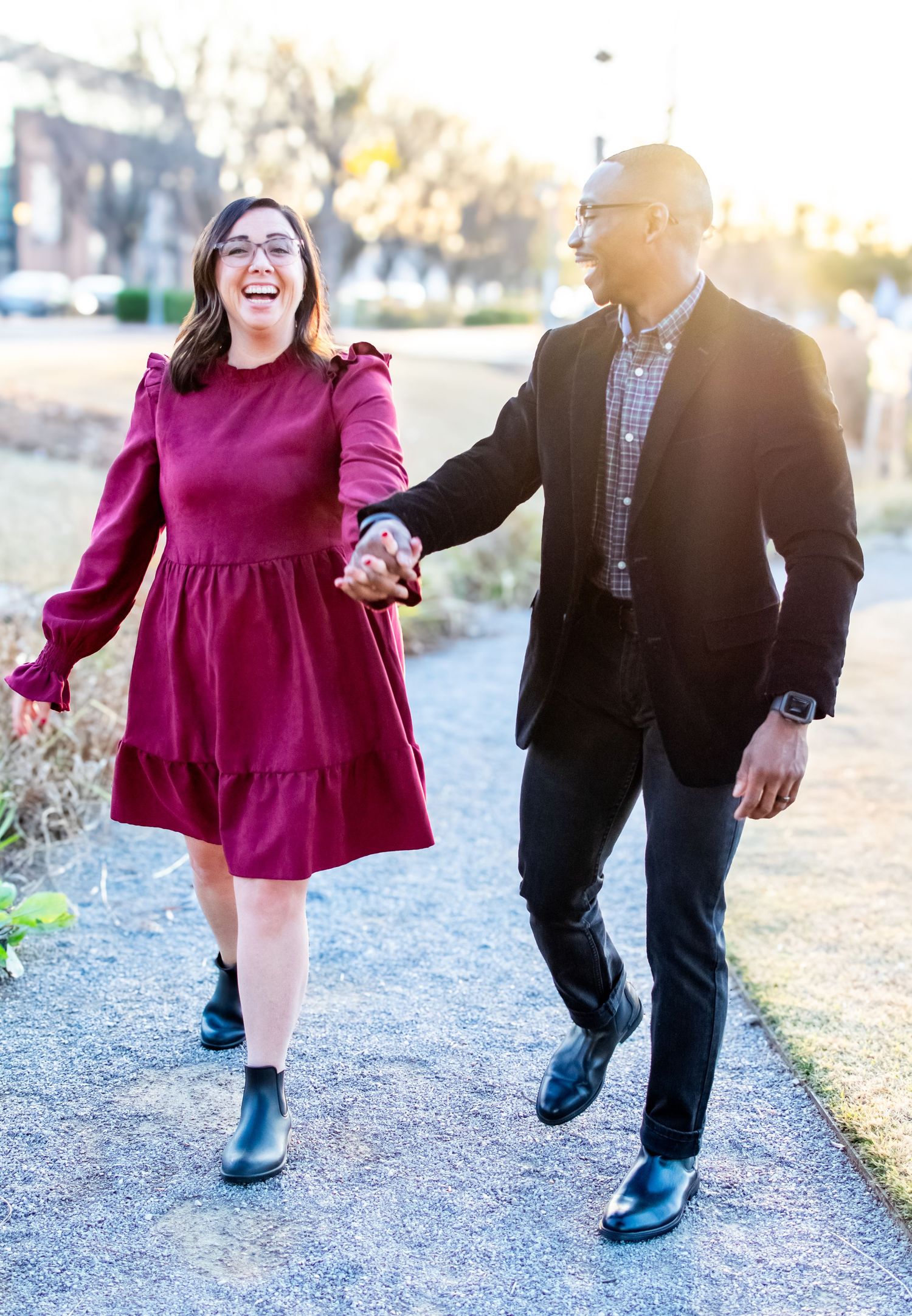 Couple walking and laughing together outdoors, wearing burgundy dress and blazer.