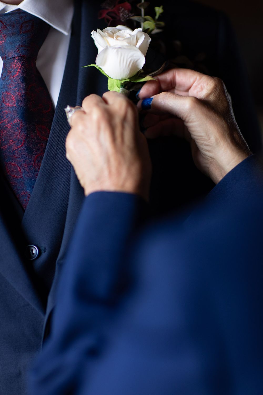 mother pinning a boutonniere to her son's suit before wedding