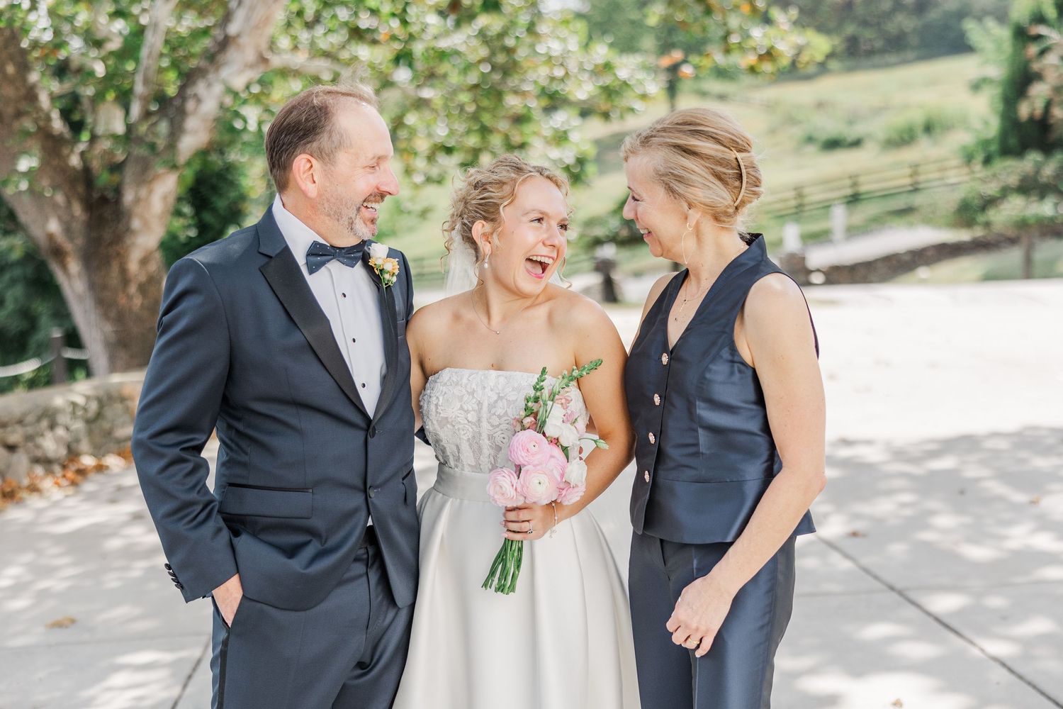 A joyful wedding moment captured outdoors with the bride in white holding a bouquet and two others in formal attire.