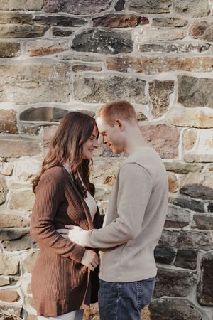 A couple shares a romantic moment against a rustic stone wall in matching brown and beige sweaters.