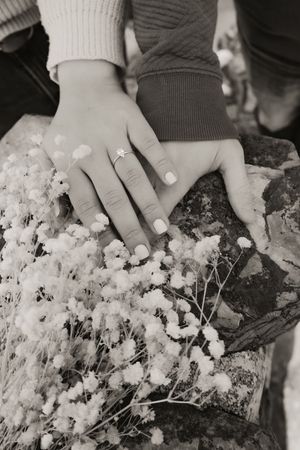 Hands delicately touch white baby's breath flowers in a black and white artistic photograph.