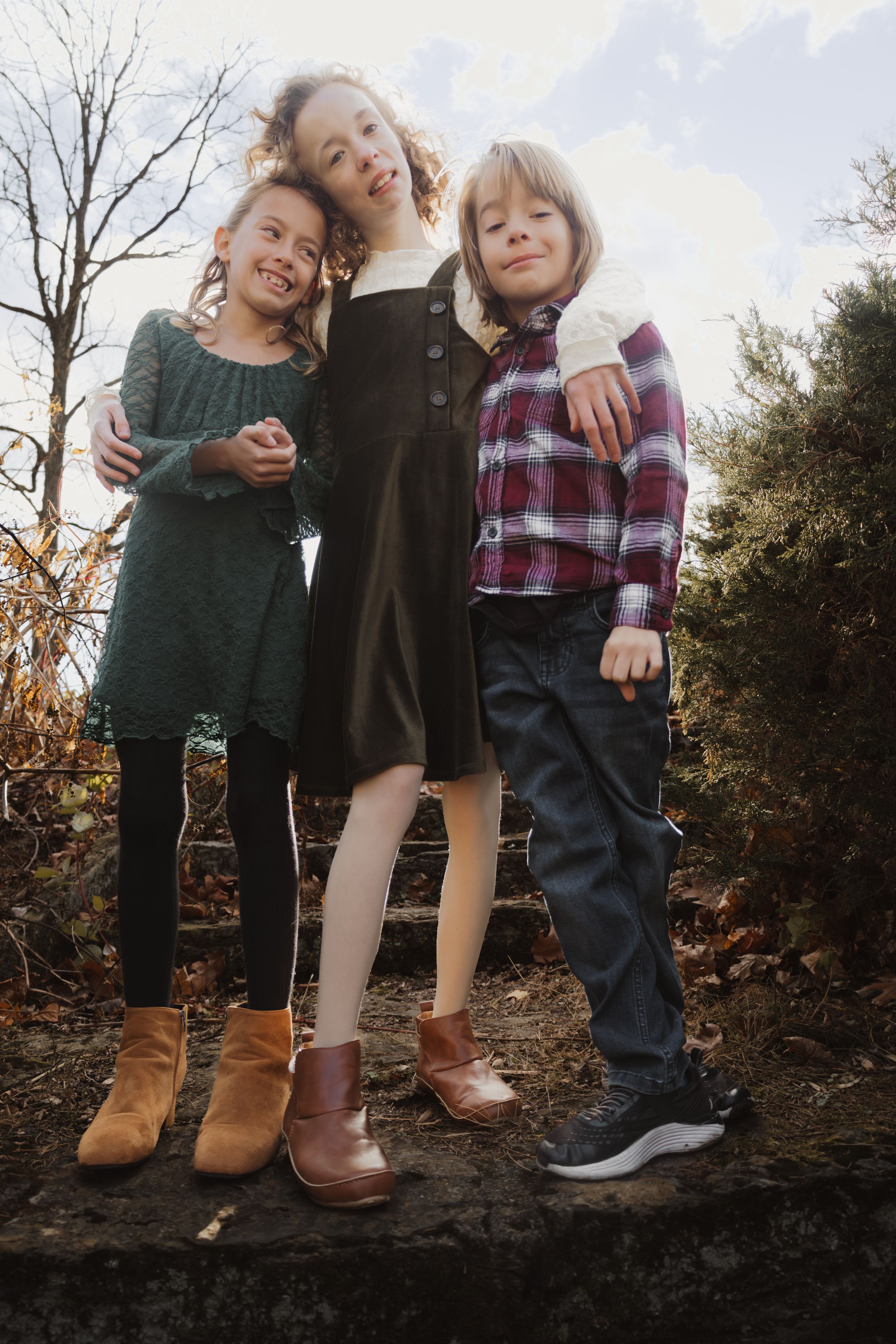 Three pairs of feet in boots and shoes standing together on a dark surface against an autumn outdoor background.
