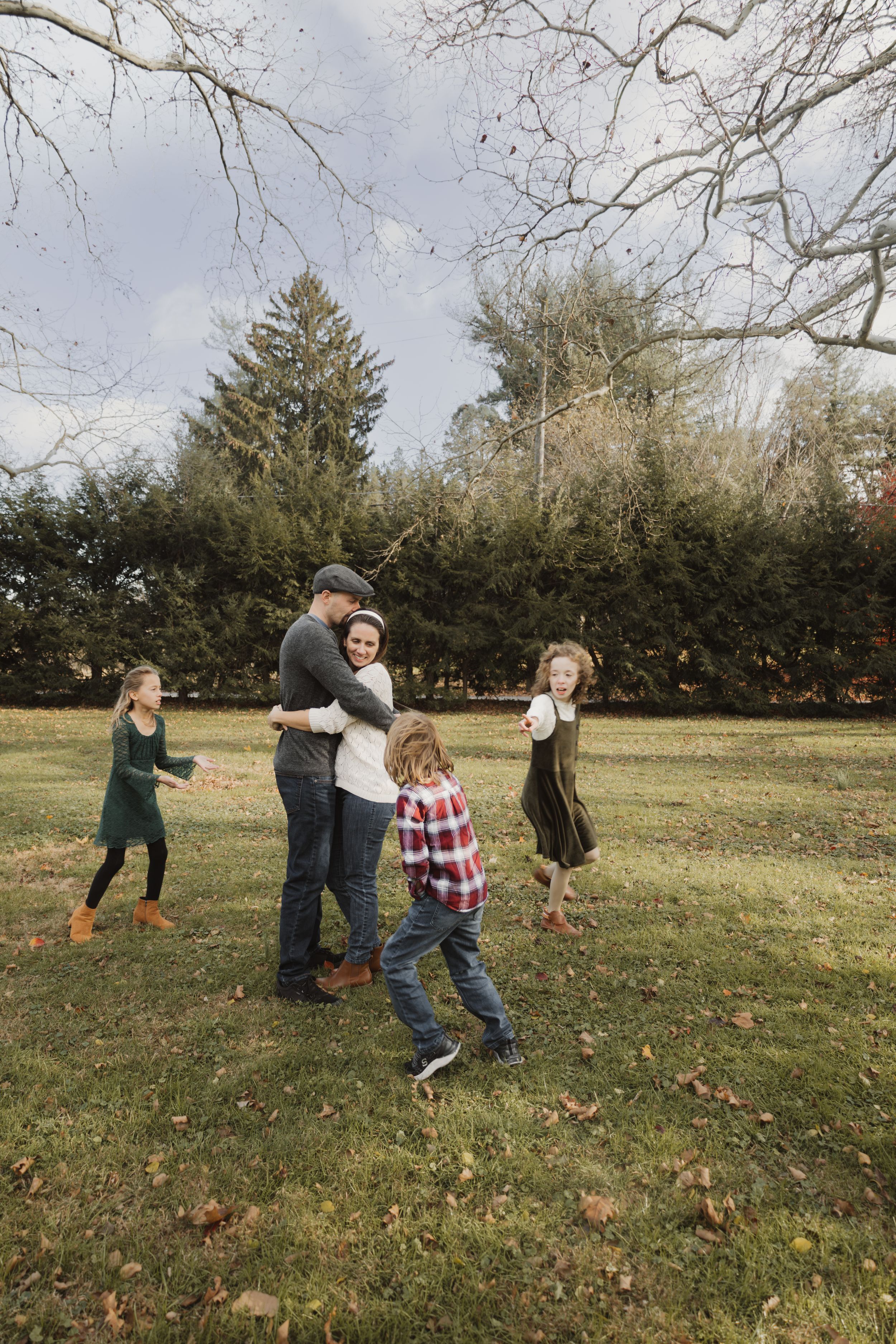 A family plays together in an autumn field with scattered pumpkins on the grass.