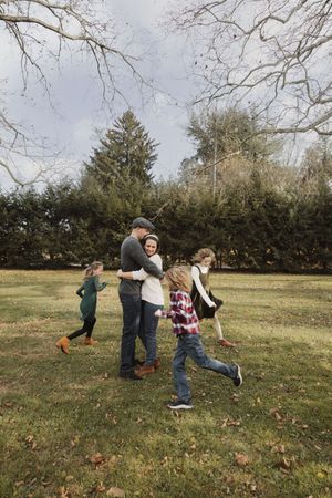 A group plays together in a grassy field on an autumn day with fallen leaves scattered on the ground.