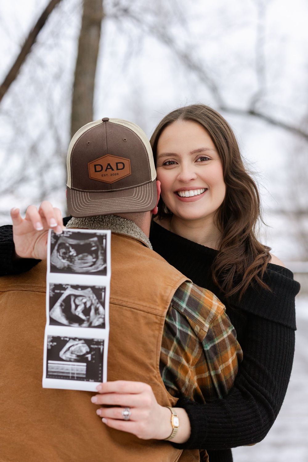 Pregnancy announcement photos showing sonogram images held against a winter forest backdrop.