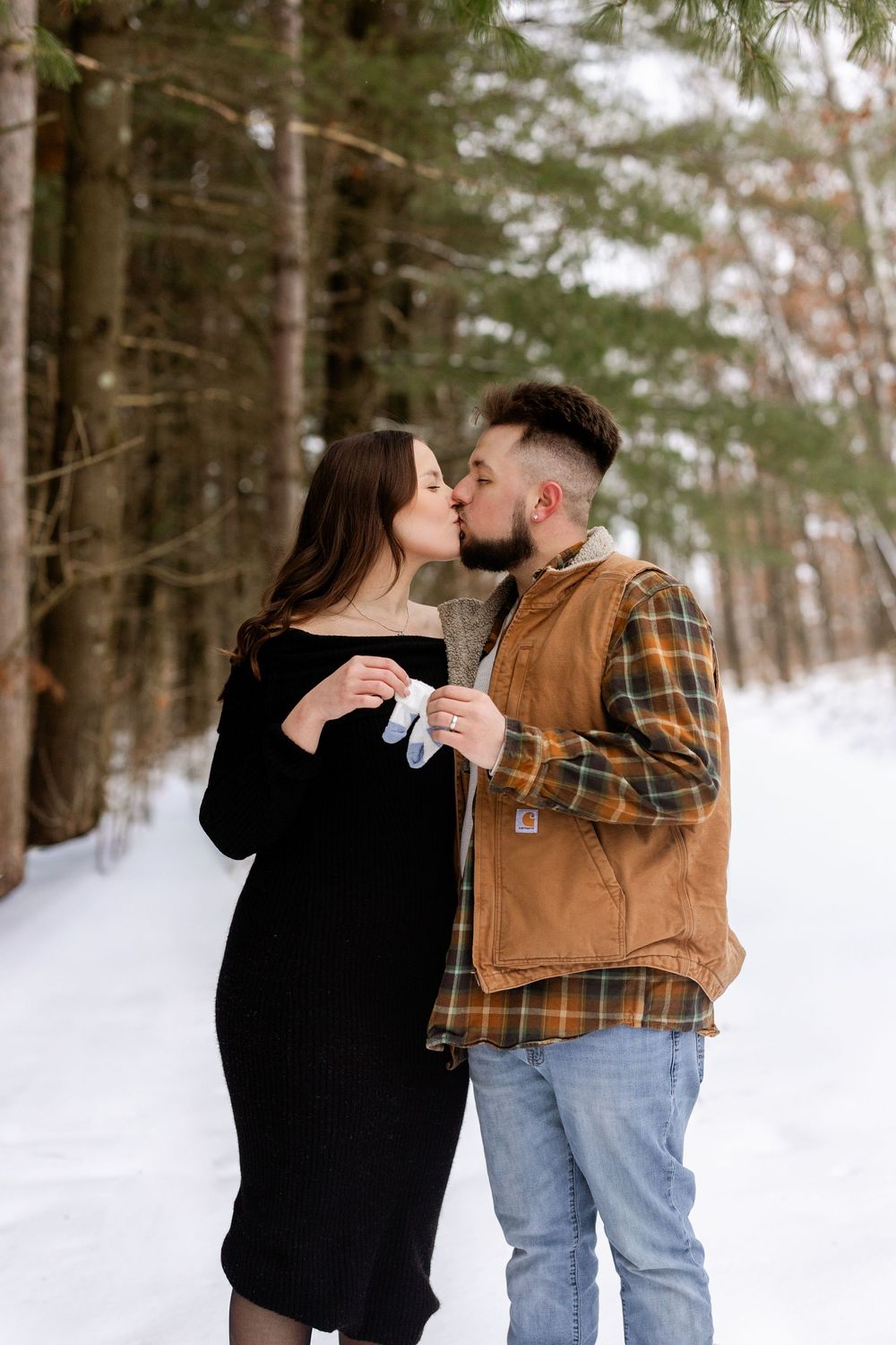 A couple shares a romantic moment while holding coffee cups in a snowy winter forest setting.