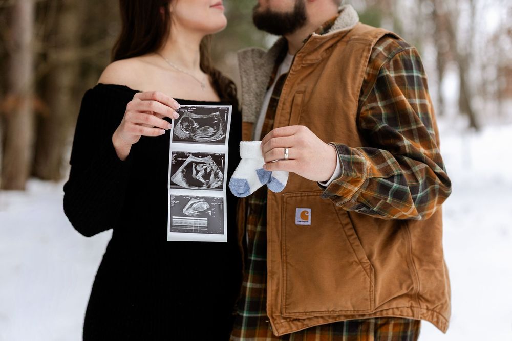 Person in brown corduroy jacket holds up ultrasound photos in snowy winter setting.
