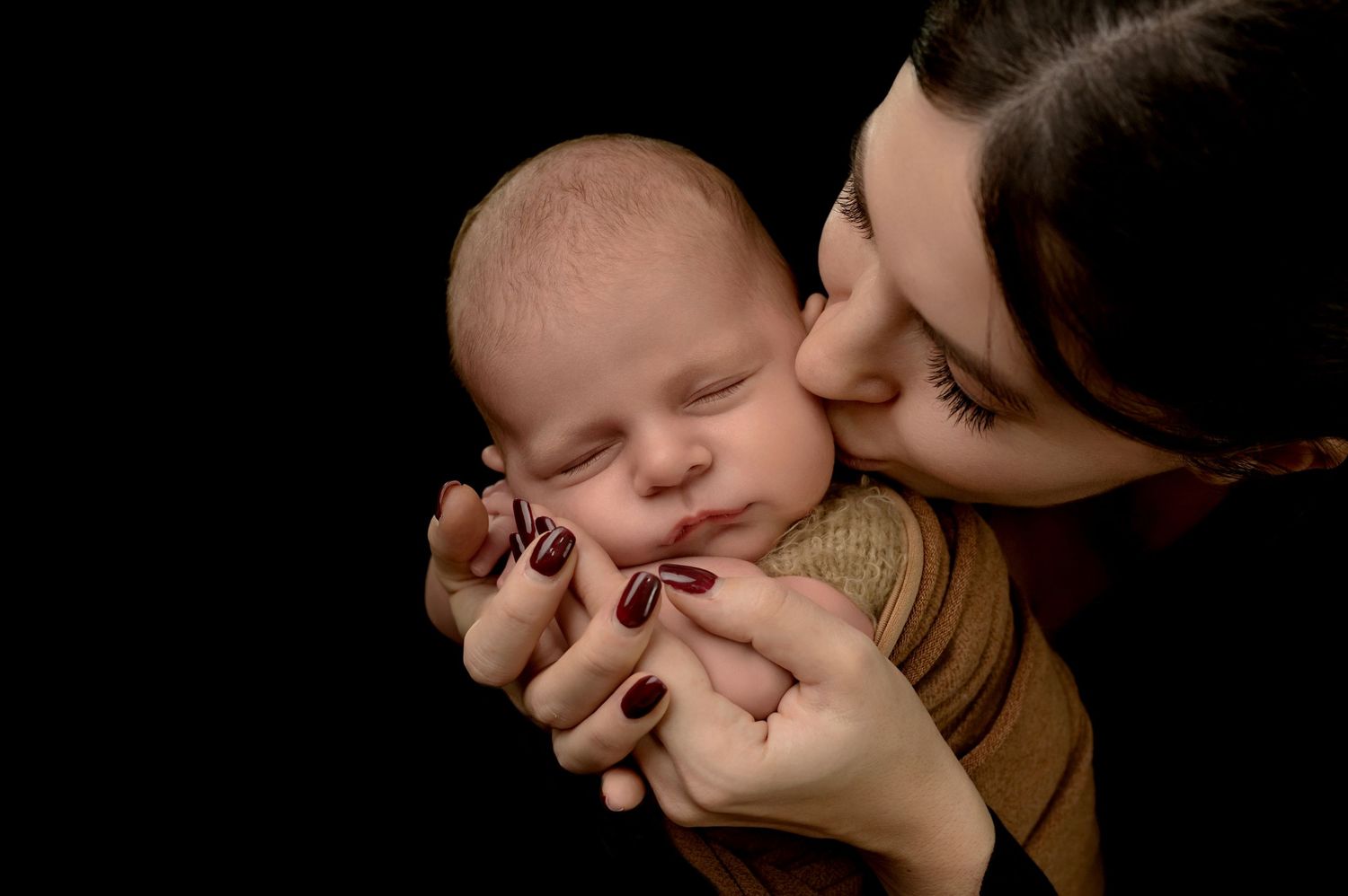 A close-up shot of a person kissing a baby's cheek in a dark, intimate setting.