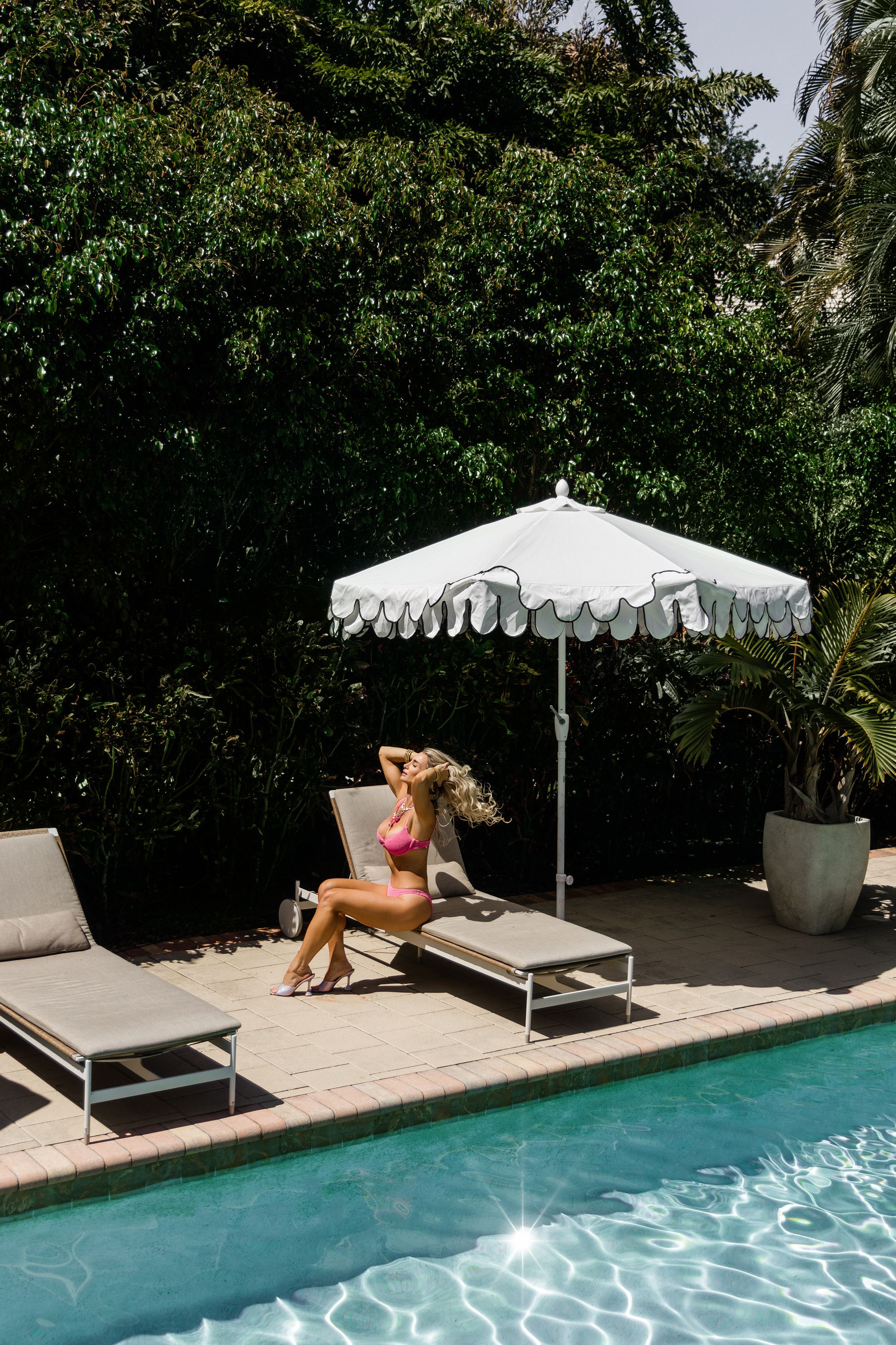Luxury poolside editorial portrait in pink swimwear and statement jewelry photographed in Jupiter Florida resort setting.