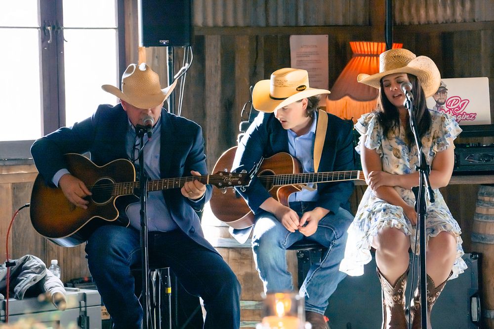 Musicians perform together with guitars and instruments in front of a rustic wood backdrop.