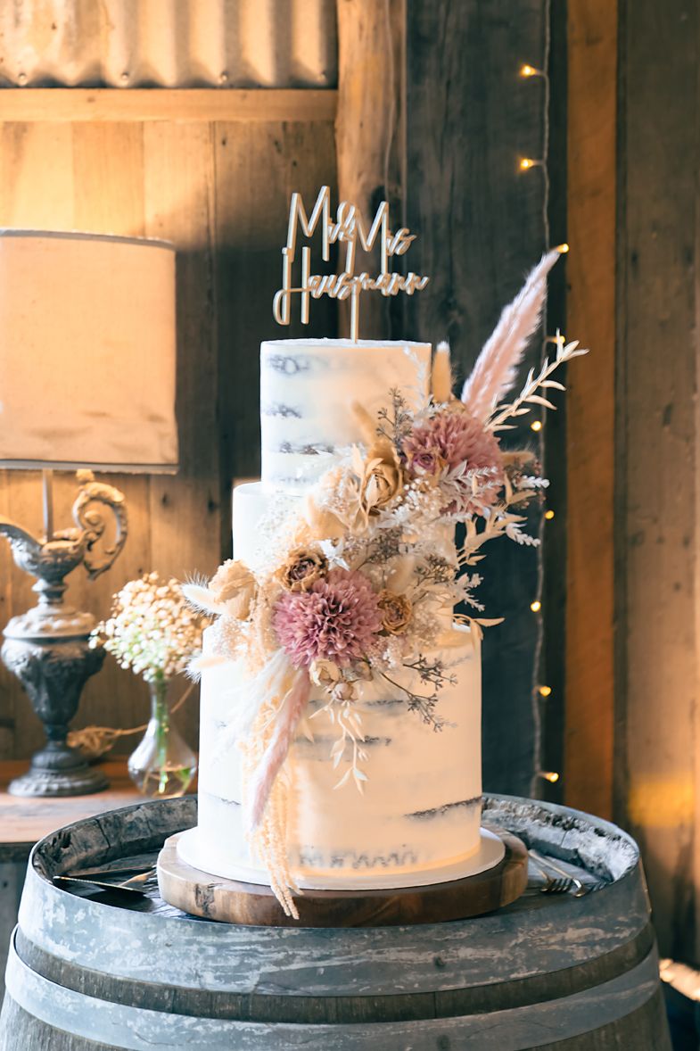 Three elegant wedding cakes adorned with delicate dried flowers and foliage displayed on rustic wooden pedestals.