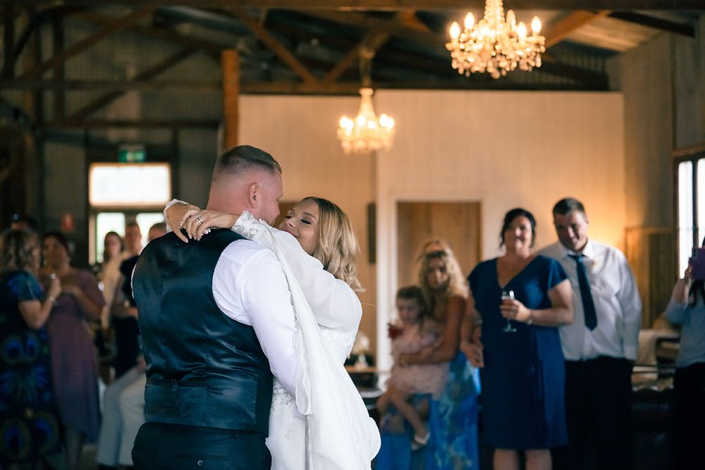 Wedding guests dance and celebrate on an elegant indoor dance floor beneath crystal chandeliers.