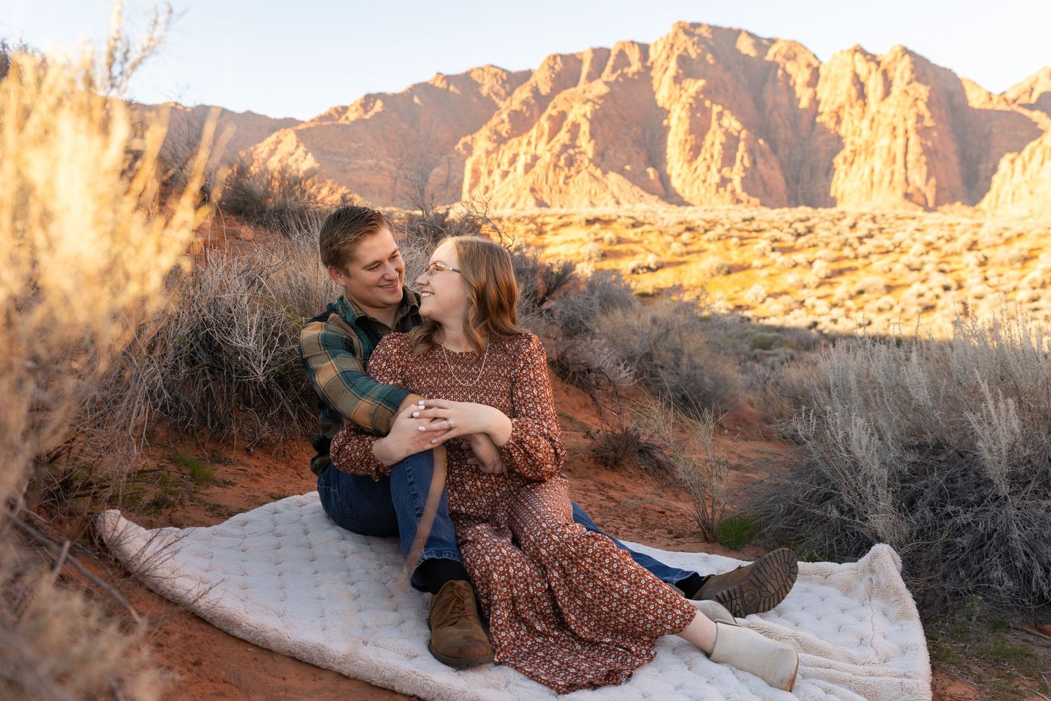 St. George utah desert with man and woman sitting on a blanket in the middle of the Desert with a beautiful red mountain in the background