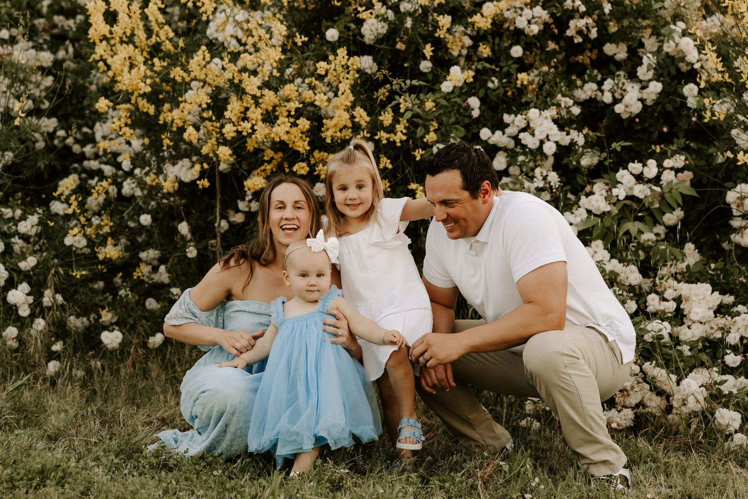 A family shares a candid moment together while sitting in front of a flowering bush.