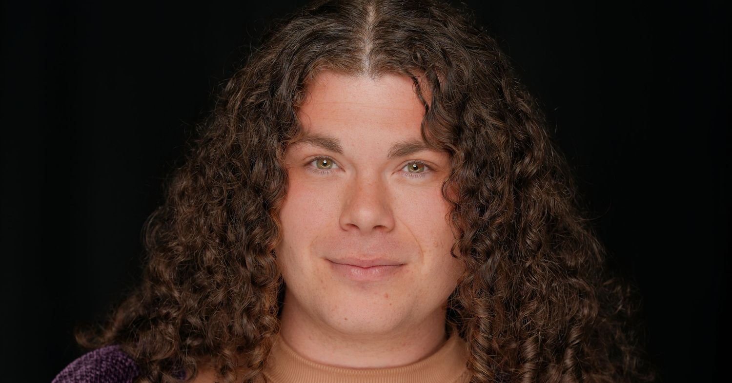 A close-up portrait of someone with long, curly dark hair against a black background.