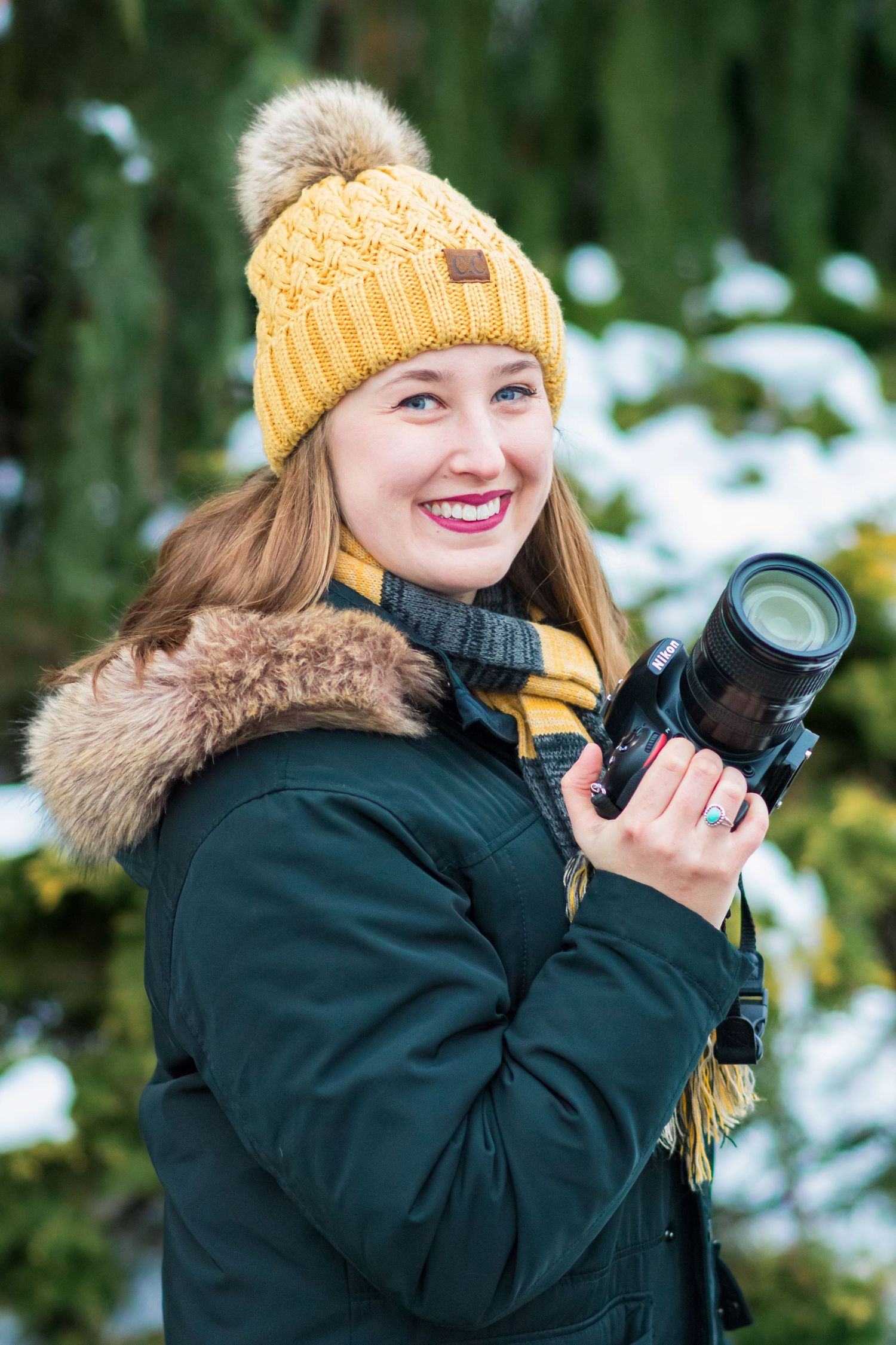 Person in winter clothing with yellow beanie taking photos outdoors in snowy conditions.