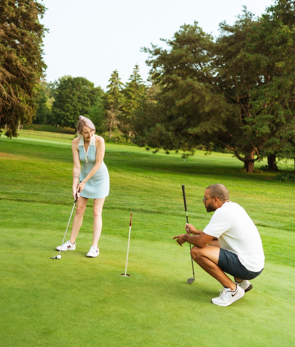Two golfers take turns analyzing and lining up their putts on a lush green golf course putting green.
