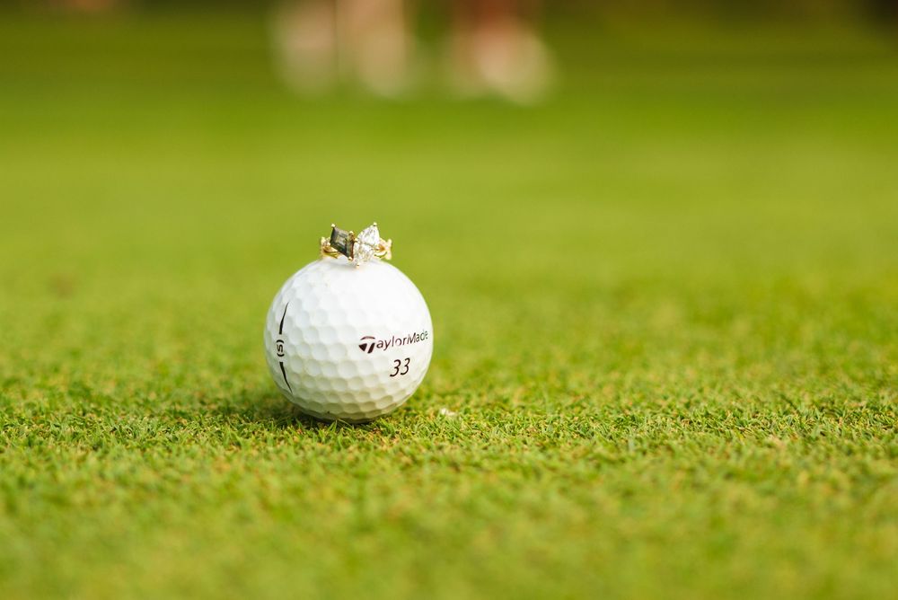 A white golf ball rests on the short-cut green grass of a golf course in bright sunlight.