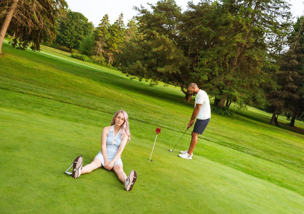 Two people enjoying a sunny day on a lush green golf course with pine trees in the background.