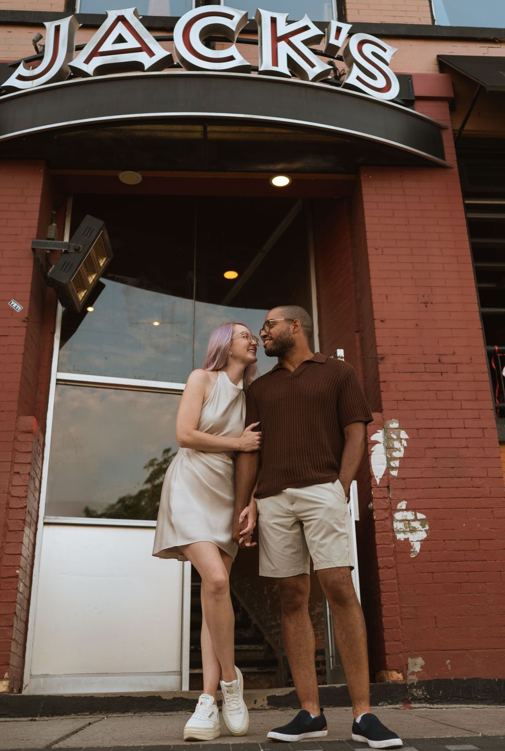 A couple shares a romantic moment outside Jack's restaurant entrance with red brick walls and illuminated signage.