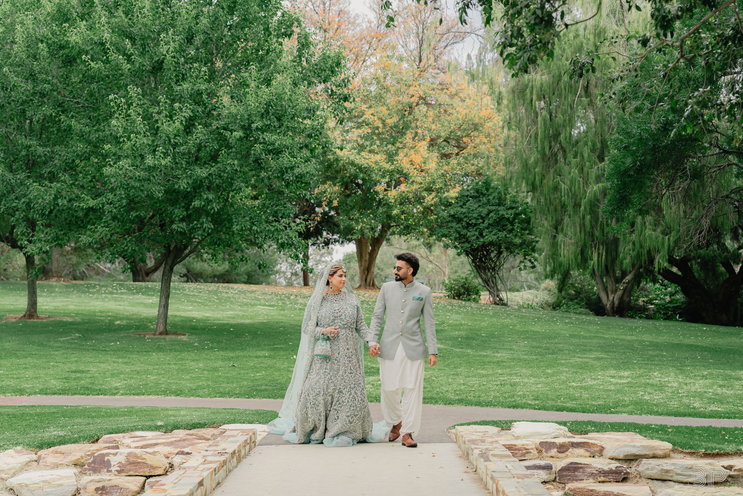 A couple stands together in a romantic garden setting with stone walls and lush greenery during an outdoor photo session.