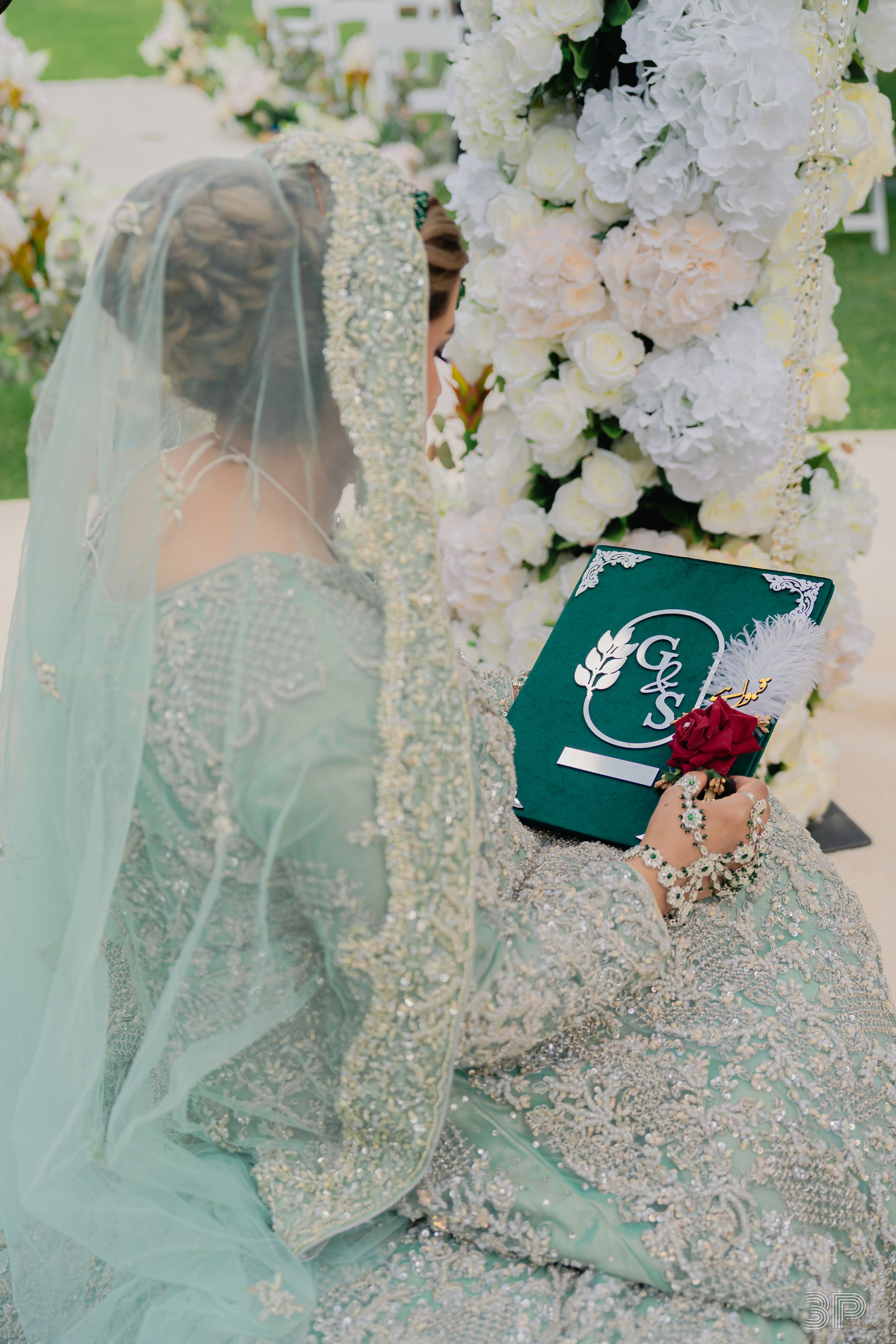 A delicate mint green lace wedding dress with veil next to an emerald green invitation with floral details.