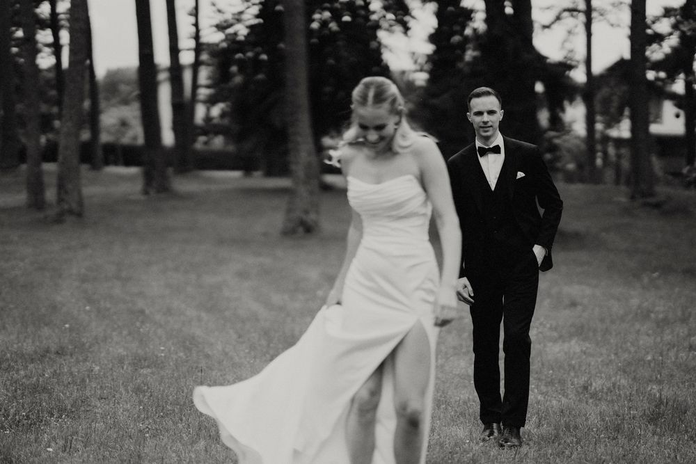 Wedding couple walks through pine forest as bride's dress flows in the wind.