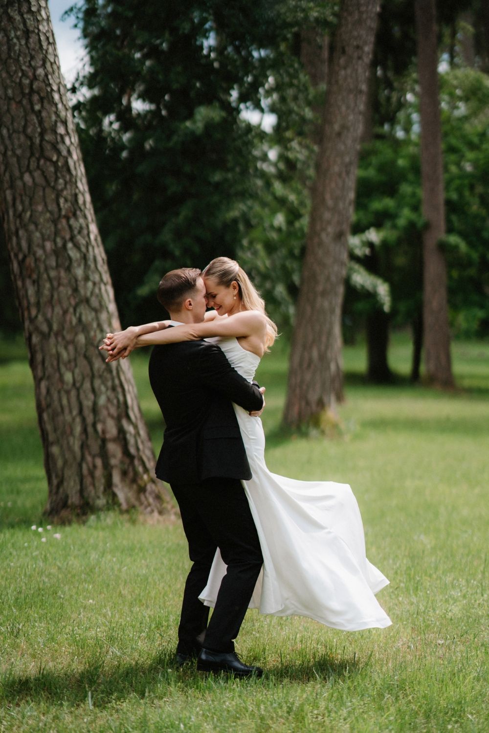 Joyful wedding moment captured as couple dances among pine trees in outdoor setting.
