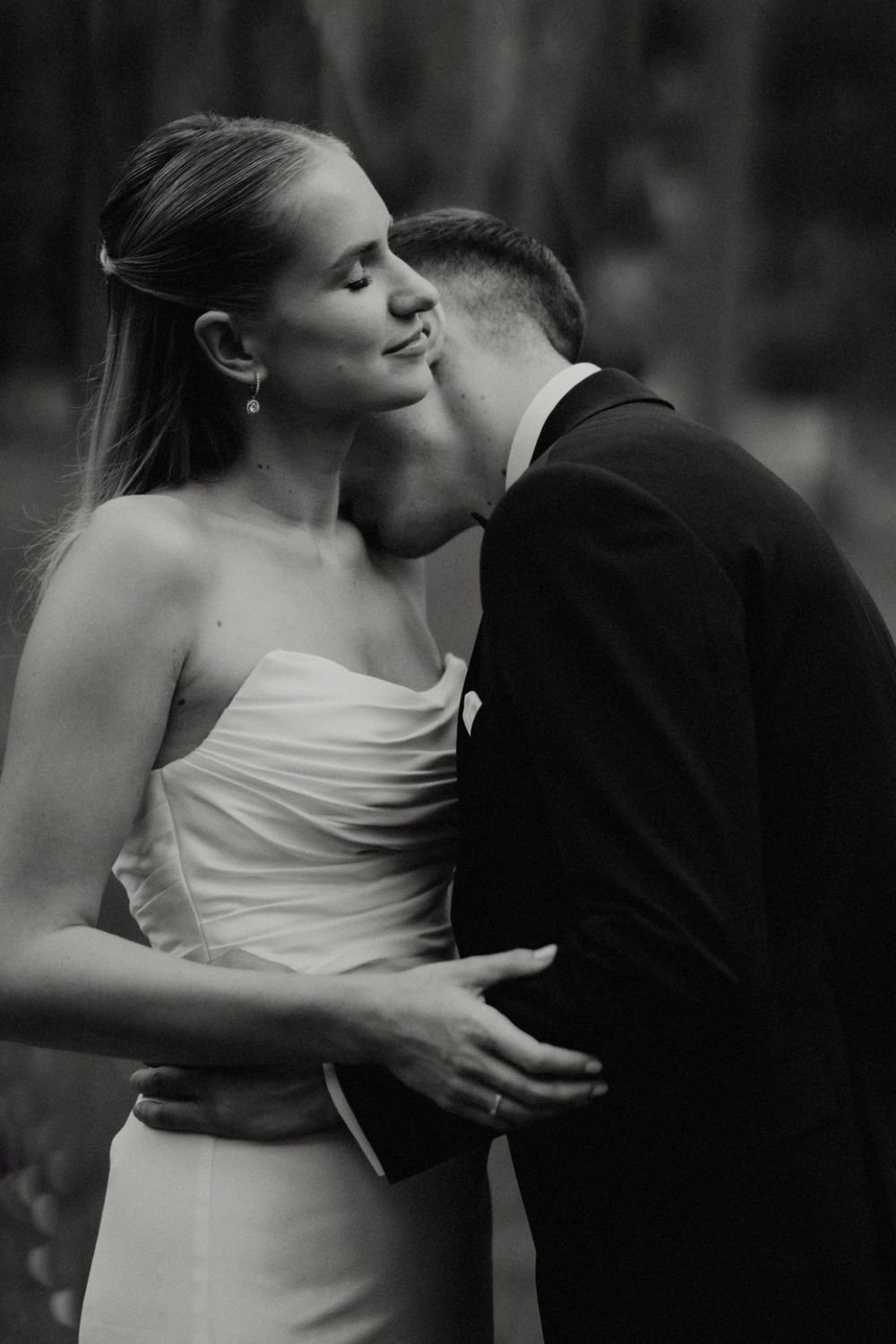 Intimate black and white portrait of couple sharing tender moment in formal wedding attire.