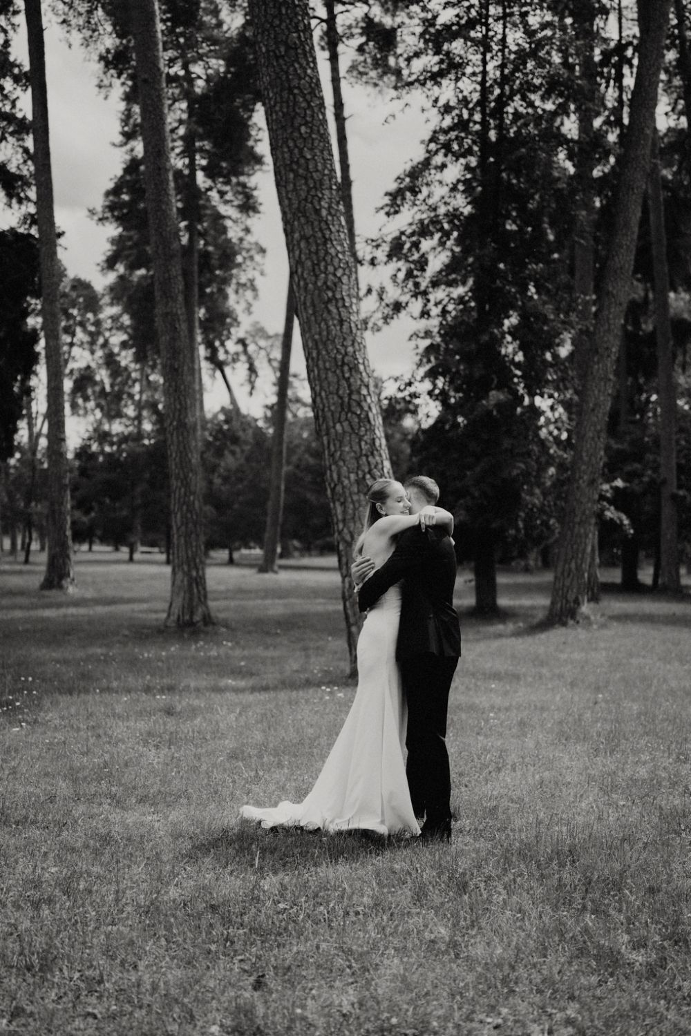 Black and white wedding photo captures couple's embrace among majestic pine trees.