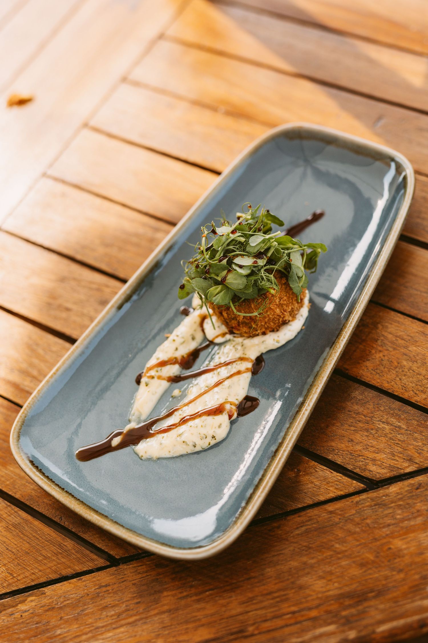Three blue ceramic plates on a wooden surface display an elegantly plated appetizer with garnish and sauce drizzle.