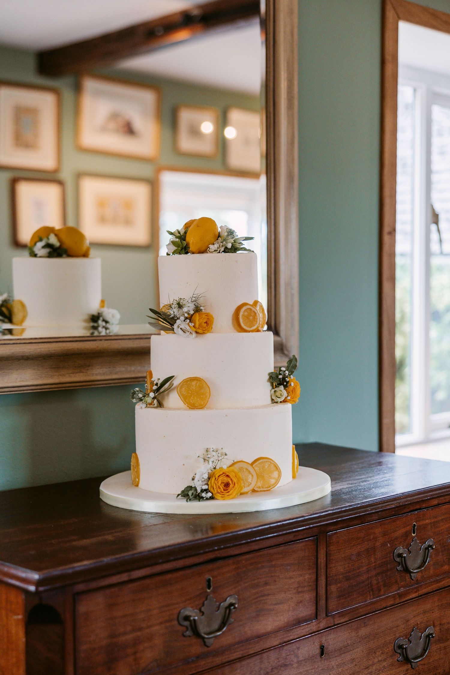 White wedding cake decorated with fresh citrus slices and greenery sits elegantly on dark wooden sideboard.