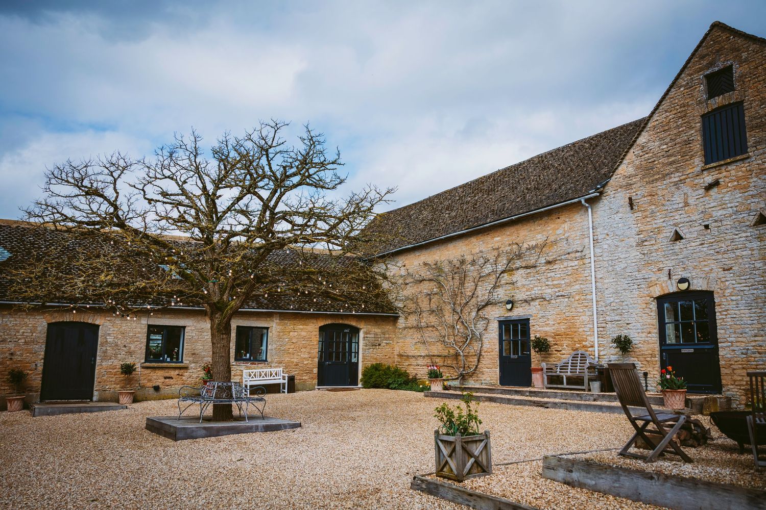 Rustic stone barn wedding venue exterior with gravel courtyard and bare winter trees against blue sky.