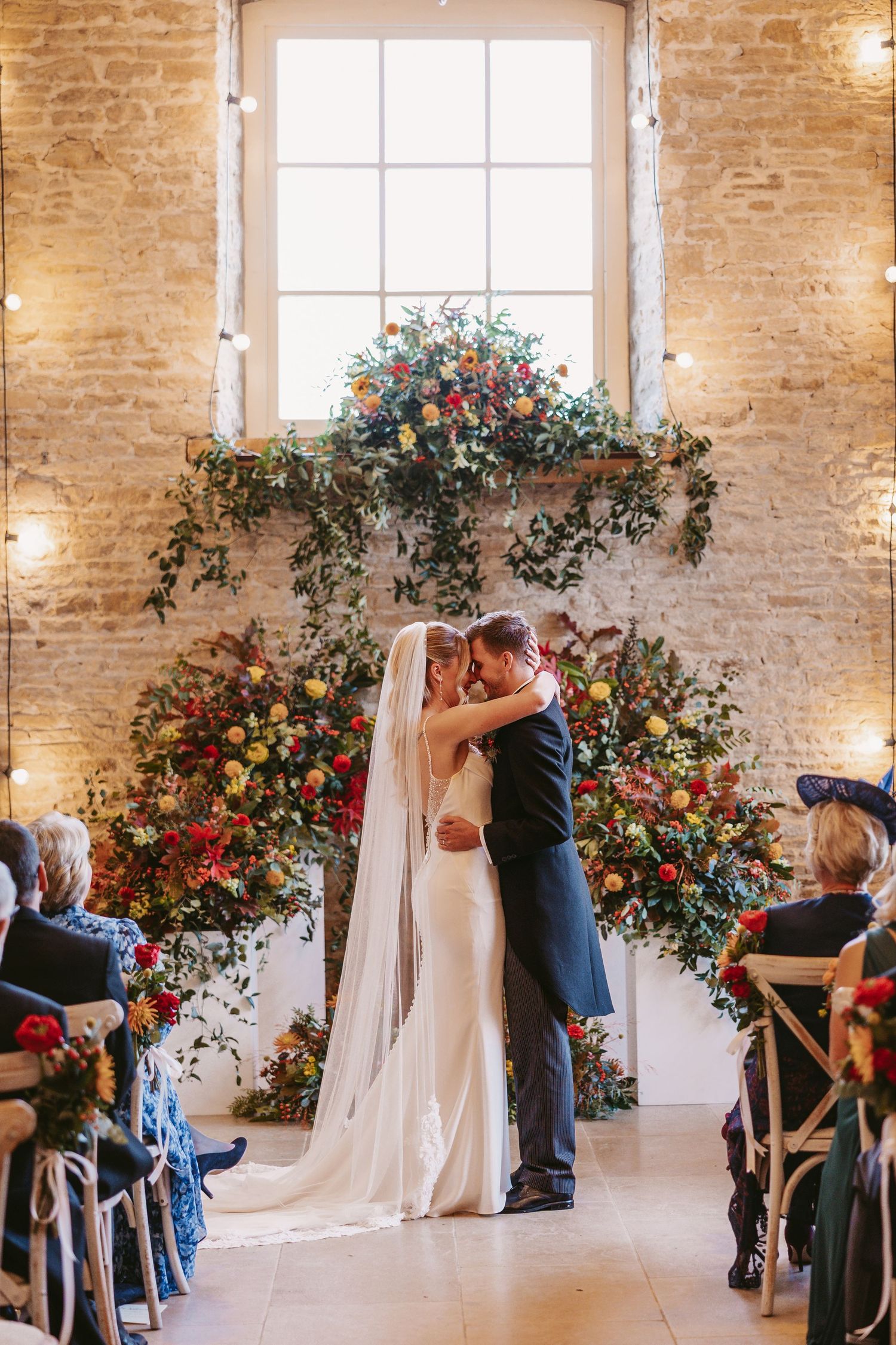 Panoramic view of an elegant indoor wedding ceremony with exposed brick walls and colorful floral arrangements by windows.