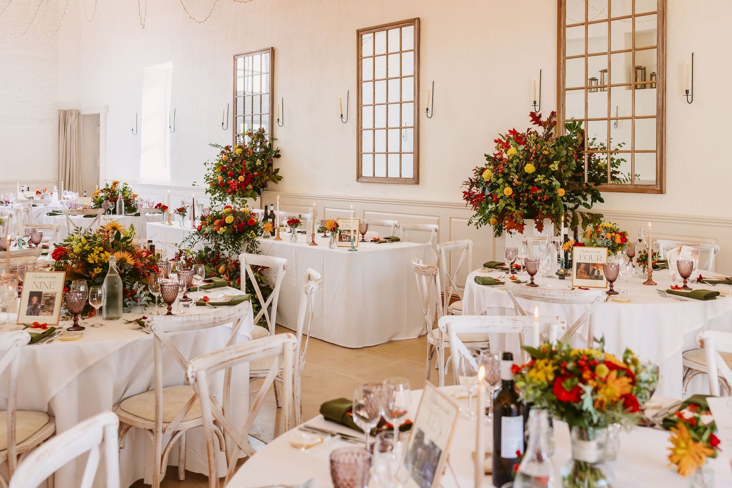 An elegant white wedding reception venue with round tables decorated with colorful floral centerpieces and rustic decor.