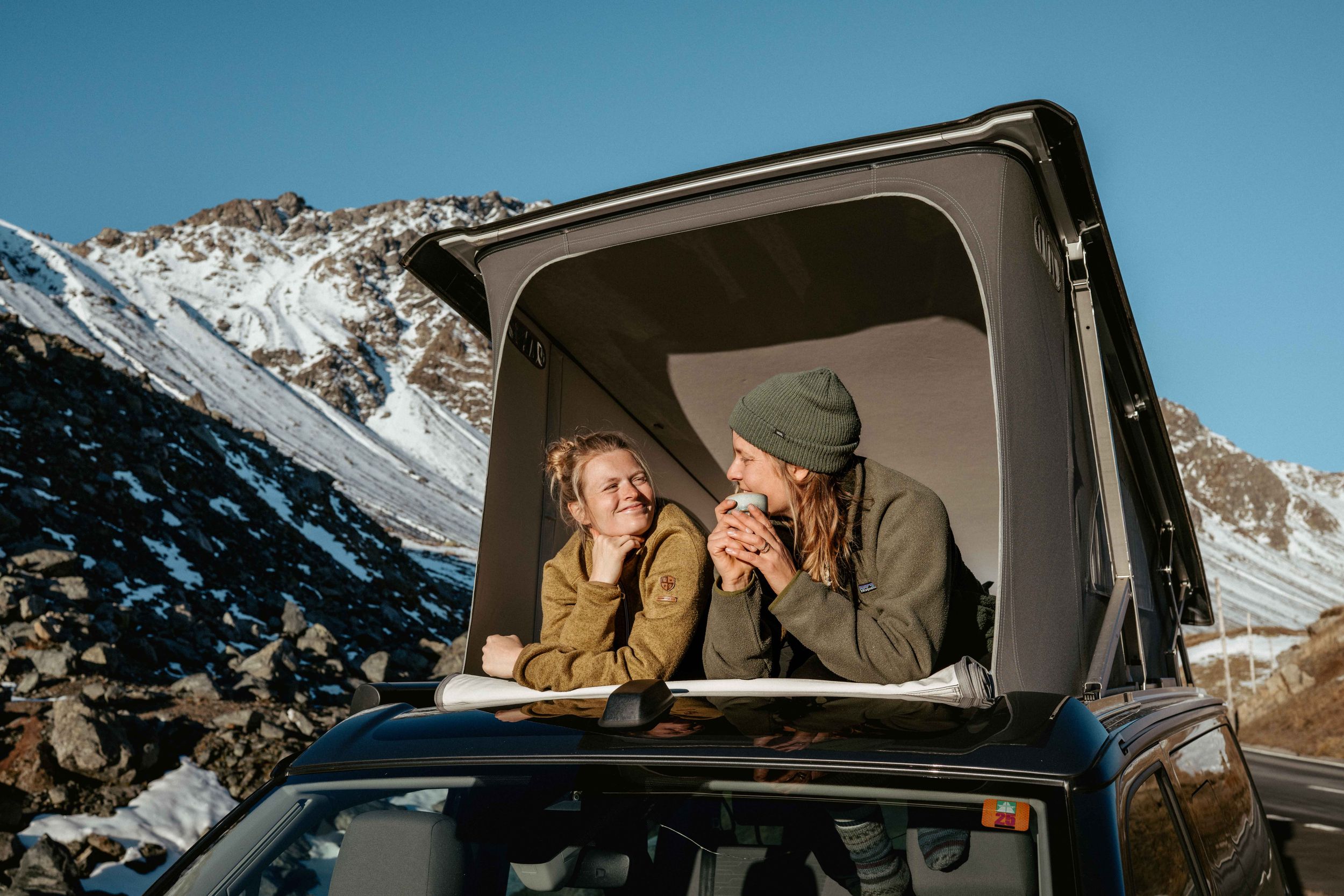 Group of friends enjoy a winter road trip through snowy mountains in a camper van during sunset.