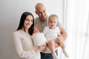 A family wearing white clothes sits together on a bed during an intimate lifestyle photoshoot.