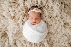 Four overhead shots of a sleeping baby wrapped in white fabric on a textured beige rug.