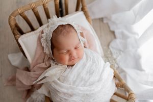 Sleeping newborn wrapped in white swaddle blanket rests peacefully in woven basket with soft lighting.
