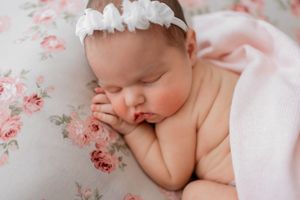 Sleeping newborn baby resting on pink floral bedding in delicate natural lighting.