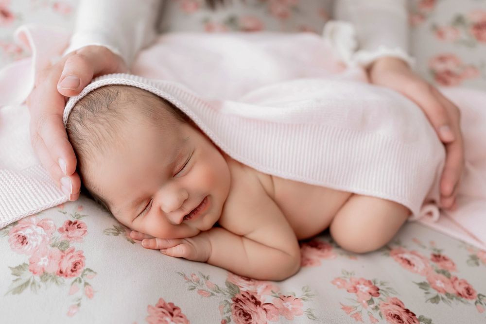 Peaceful newborn baby sleeping on pink floral fabric with soft white blanket.