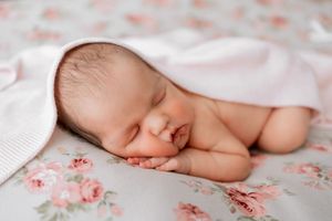 Close-up view of a sleeping newborn baby wrapped in soft white blankets on a floral patterned fabric.