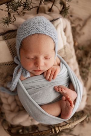 A sleeping newborn wrapped in soft gray fabric and knit hat lies peacefully in a basket during a professional photo session.